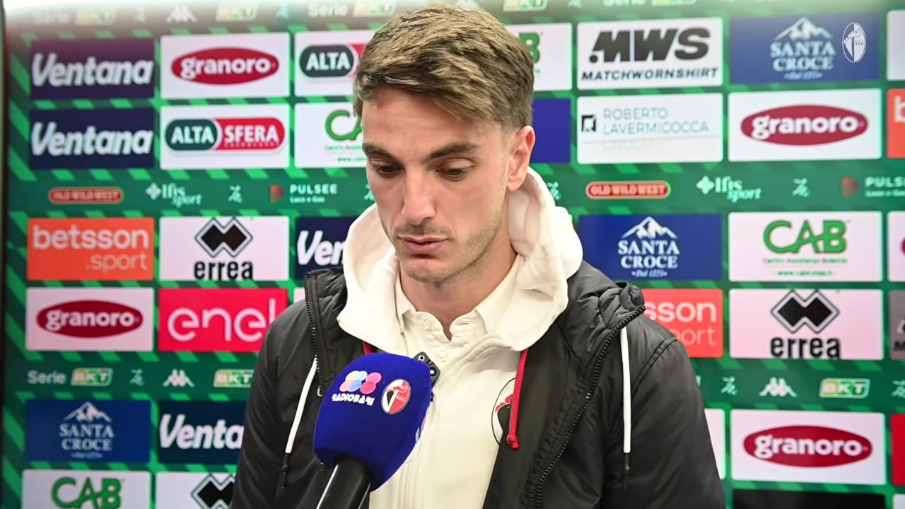 Giocatore al microfono davanti a backdrop sponsor